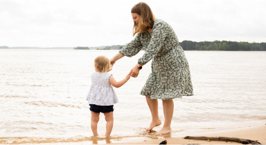 Emily and her young daughter Isla, both living with XLH, holding hands on the beach