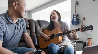 Woman playing guitar across from man on a couch